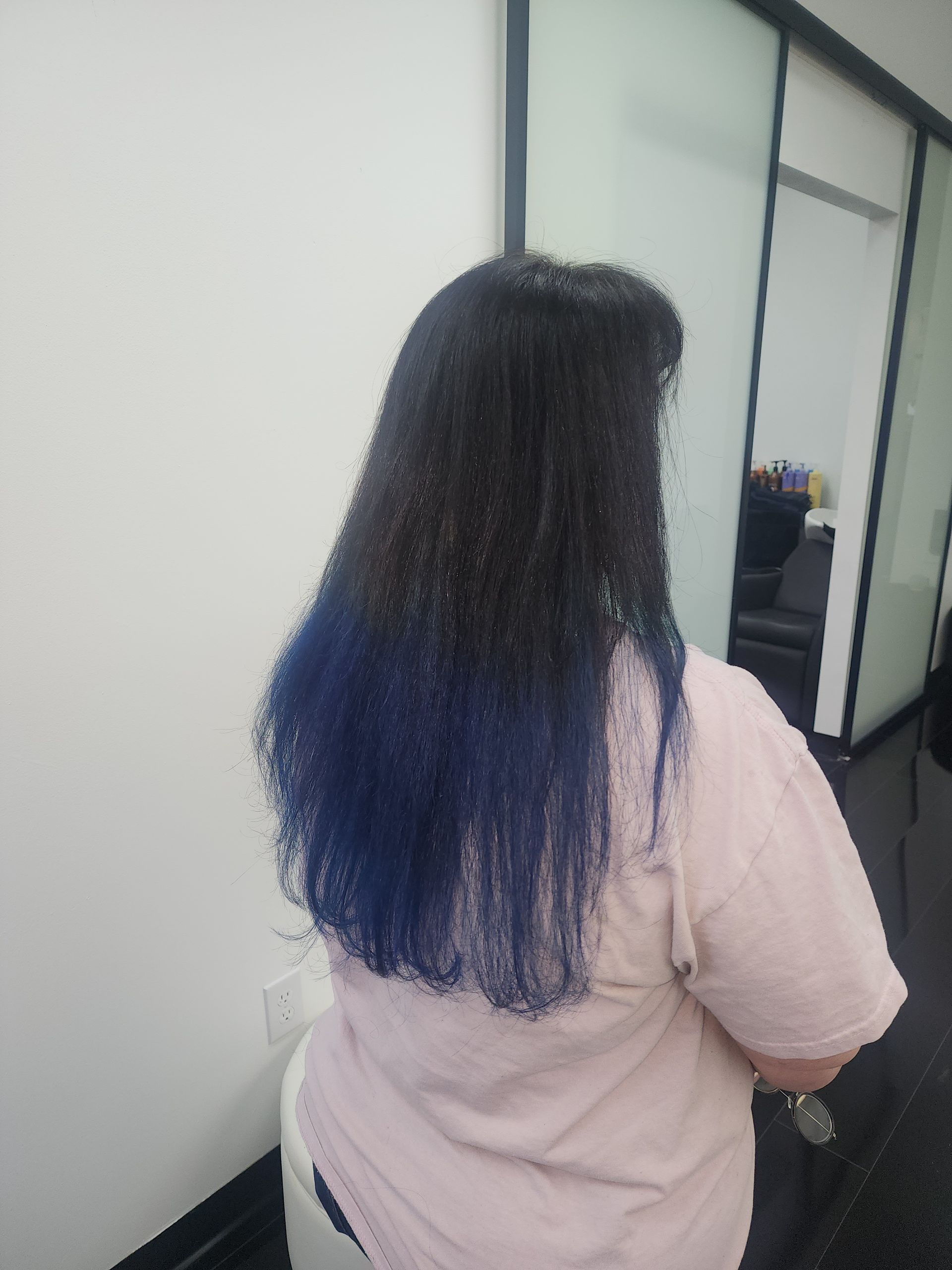 A woman with blue hair is standing in front of a mirror.
