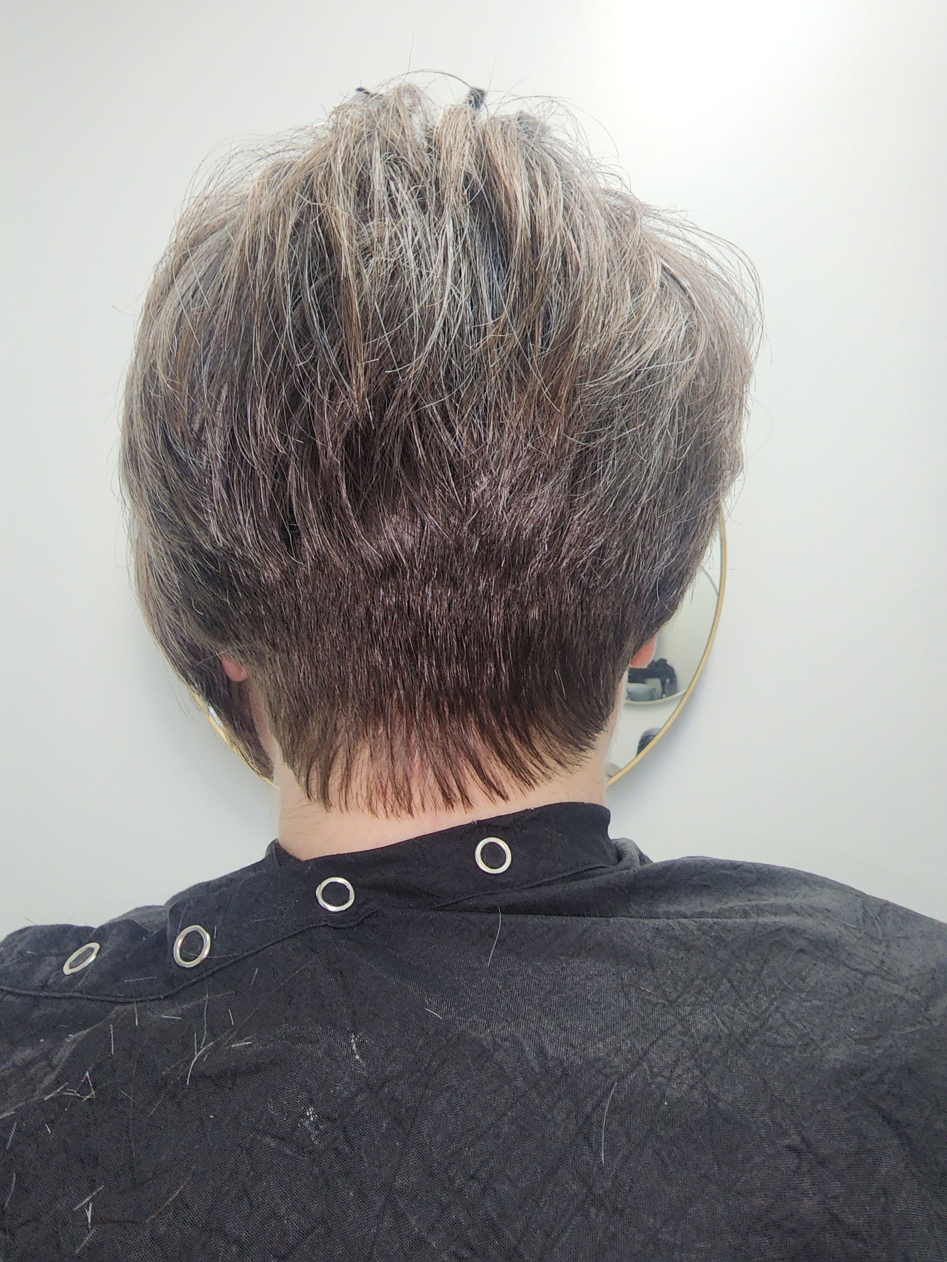 The back of a person 's head with short hair and a black shirt.