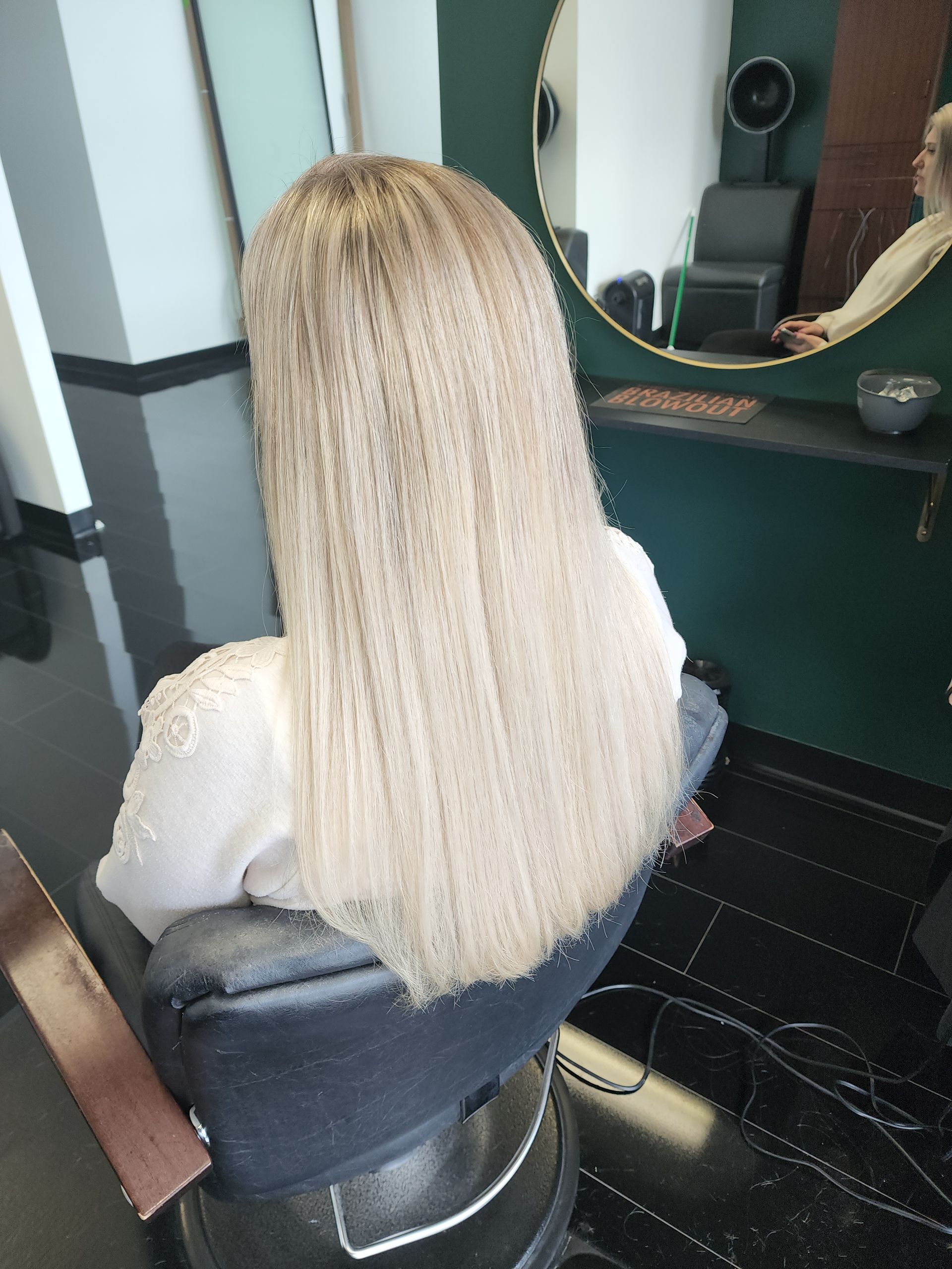 A woman is sitting in a chair in front of a mirror in a salon.
