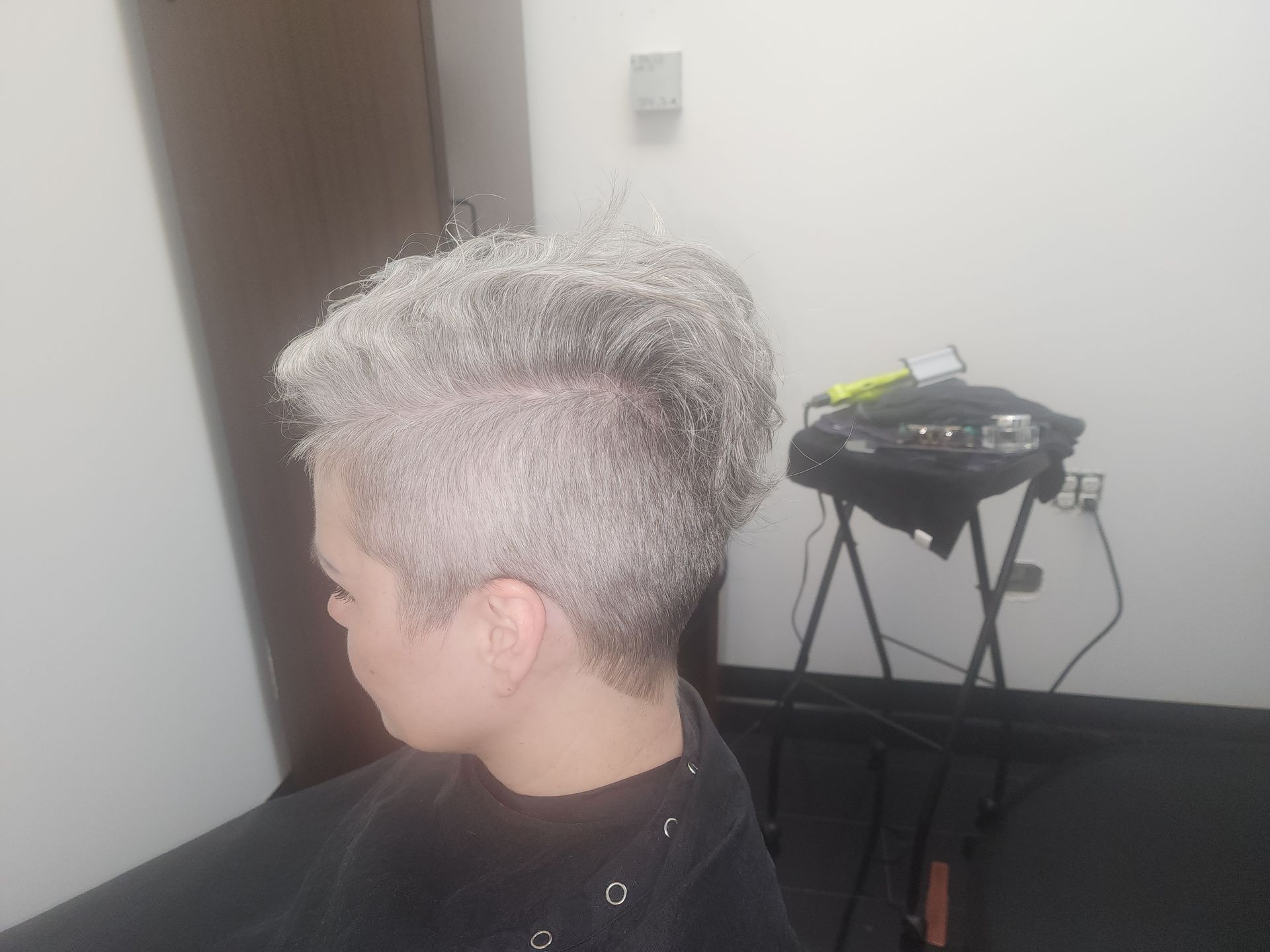 A woman with gray hair is getting her hair cut in a salon.