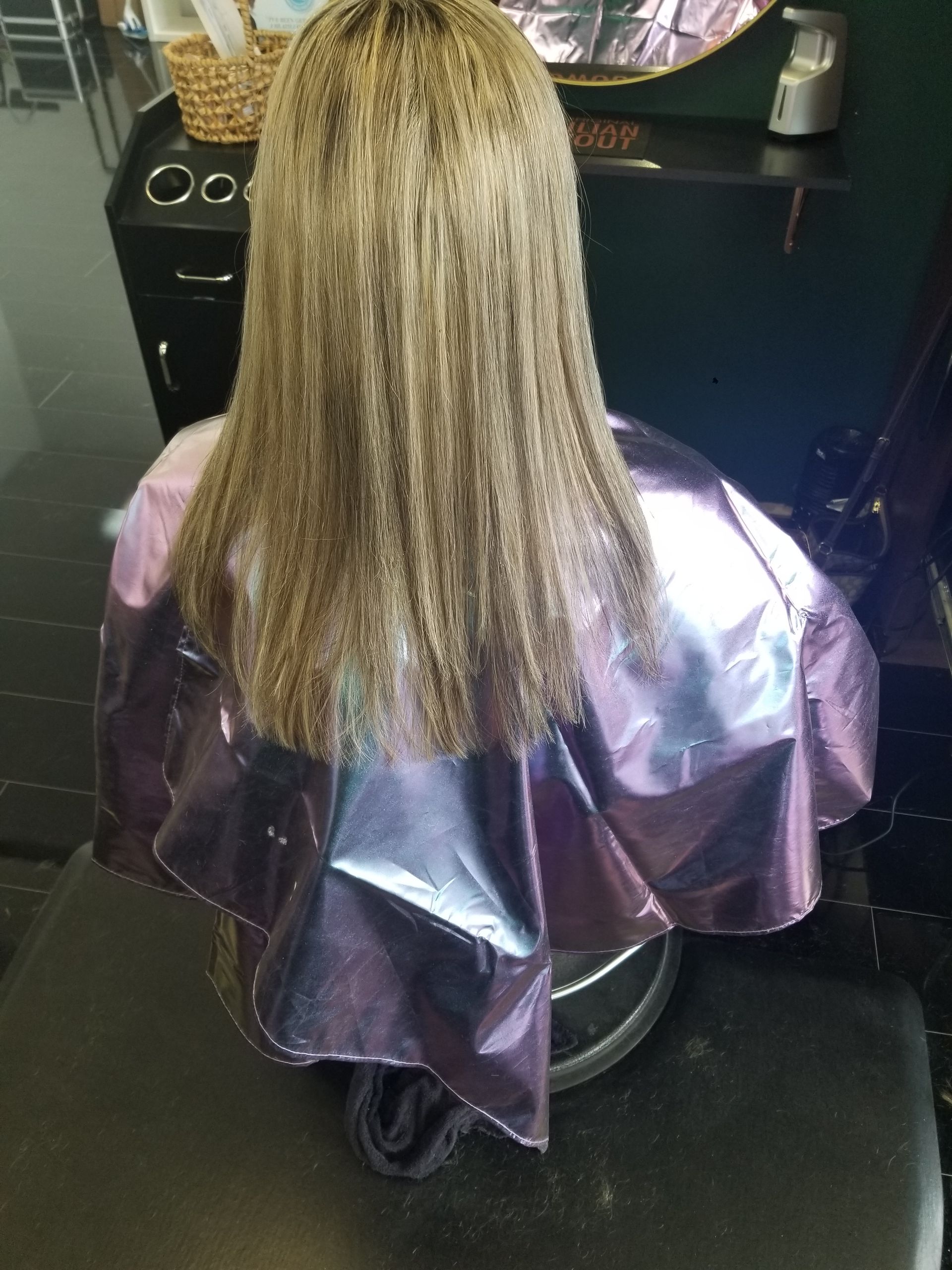 A woman is sitting in a chair with a purple cape on her head.