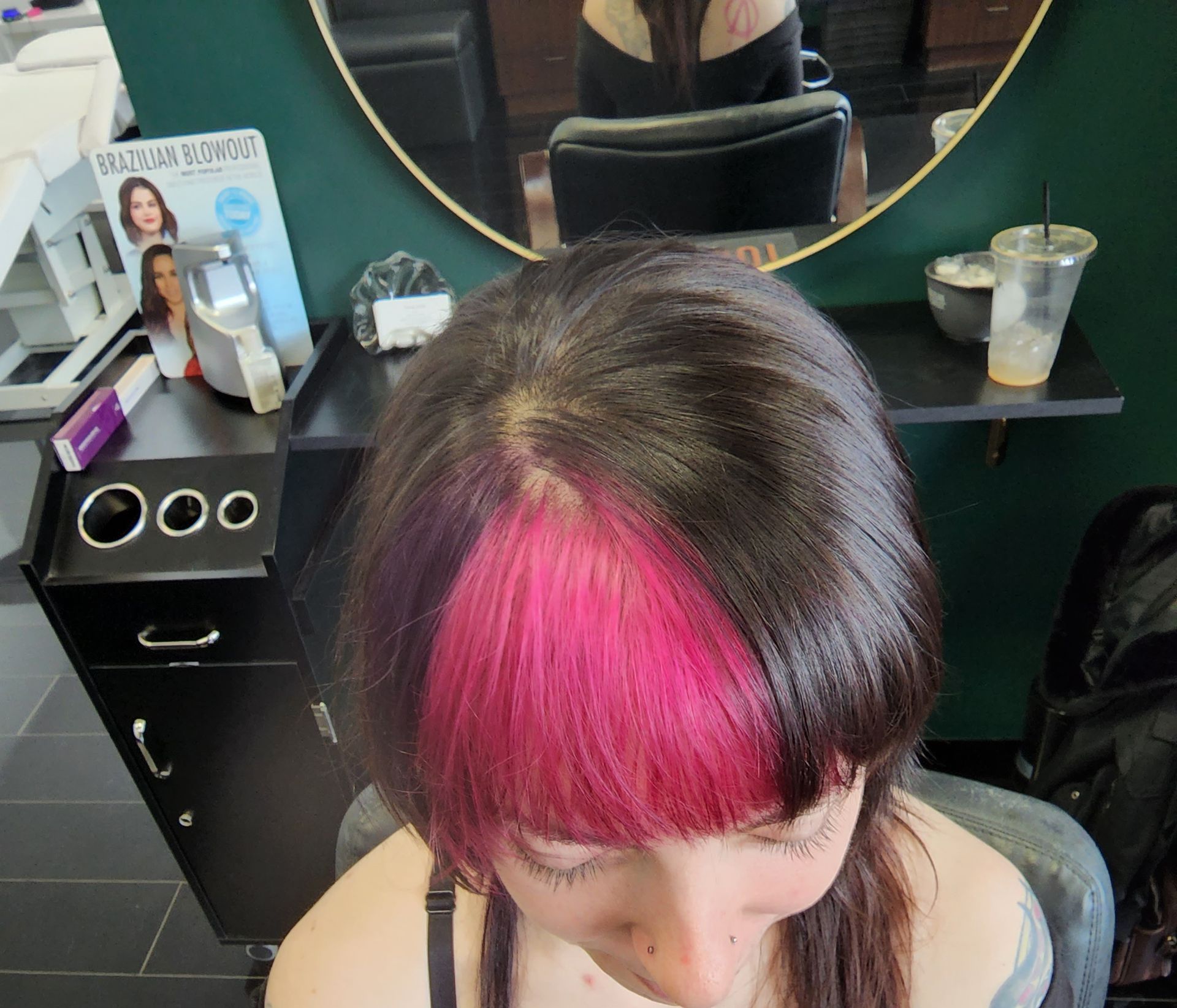 A woman with pink hair is sitting in front of a mirror