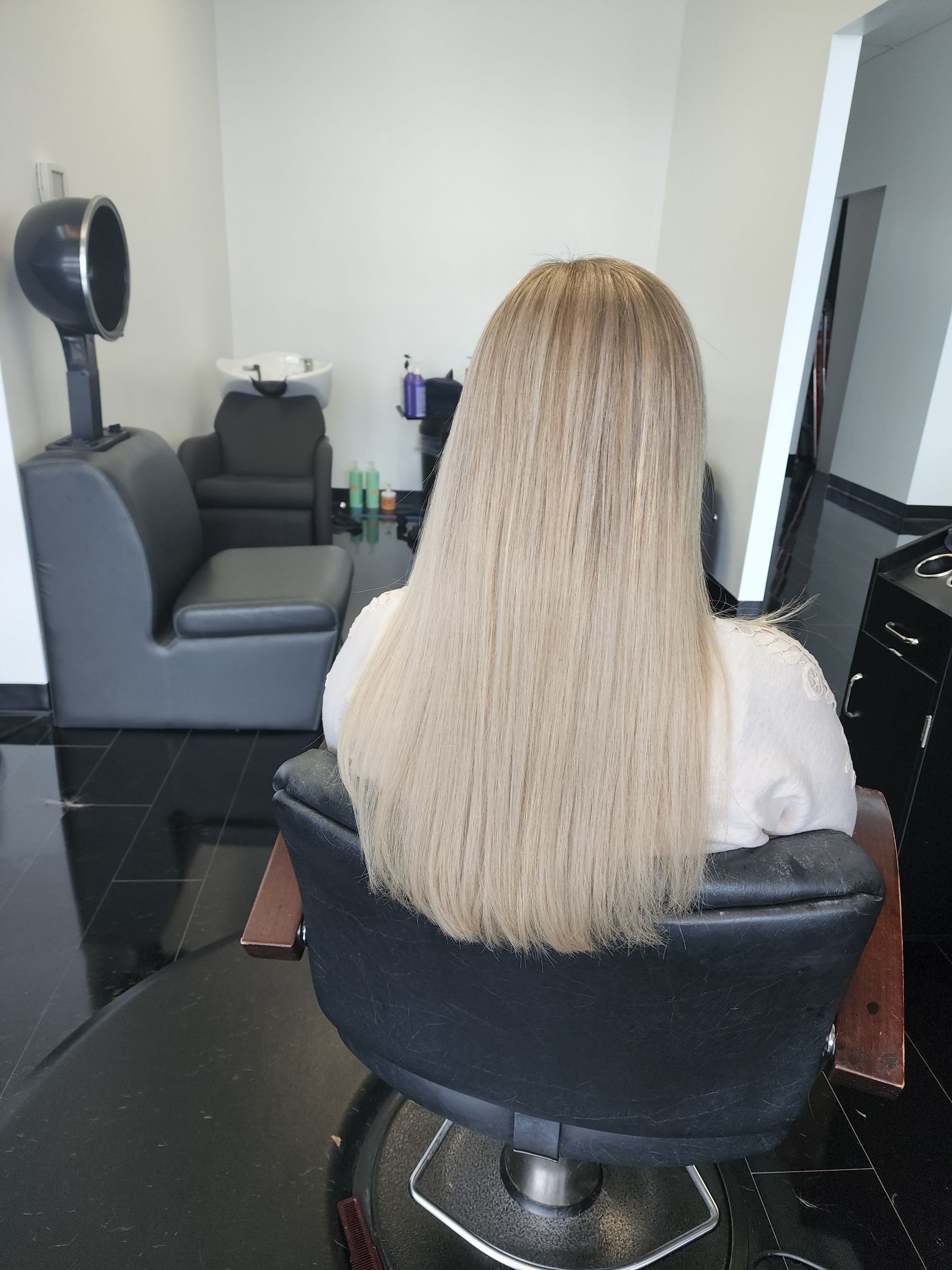 A woman with long blonde hair is sitting in a chair in a salon.