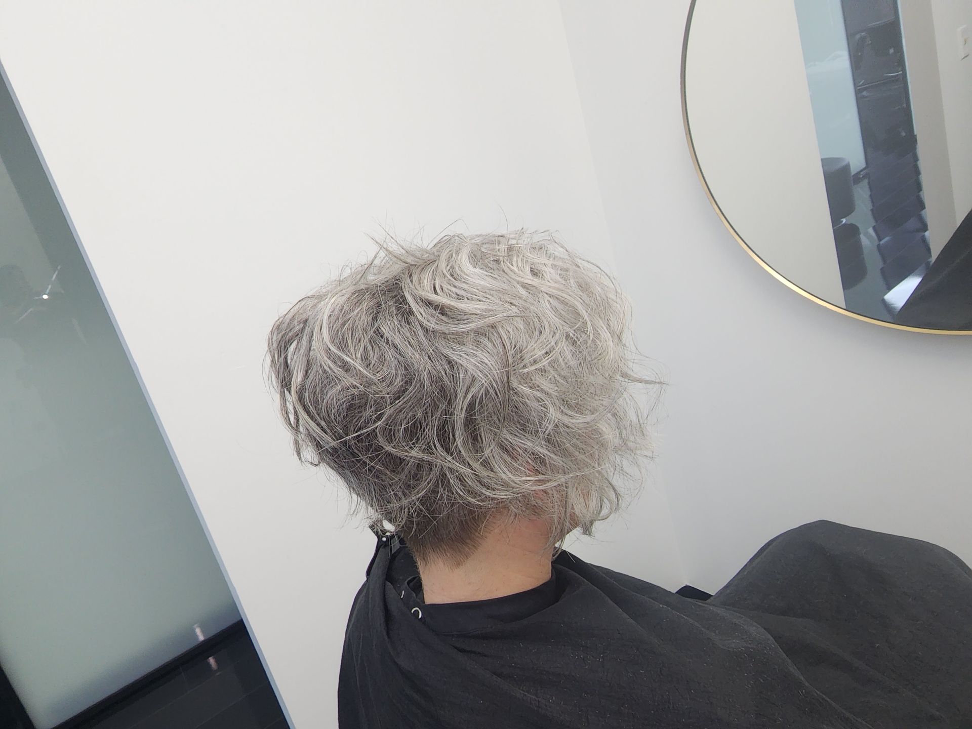A woman with gray hair is sitting in a chair in front of a mirror.
