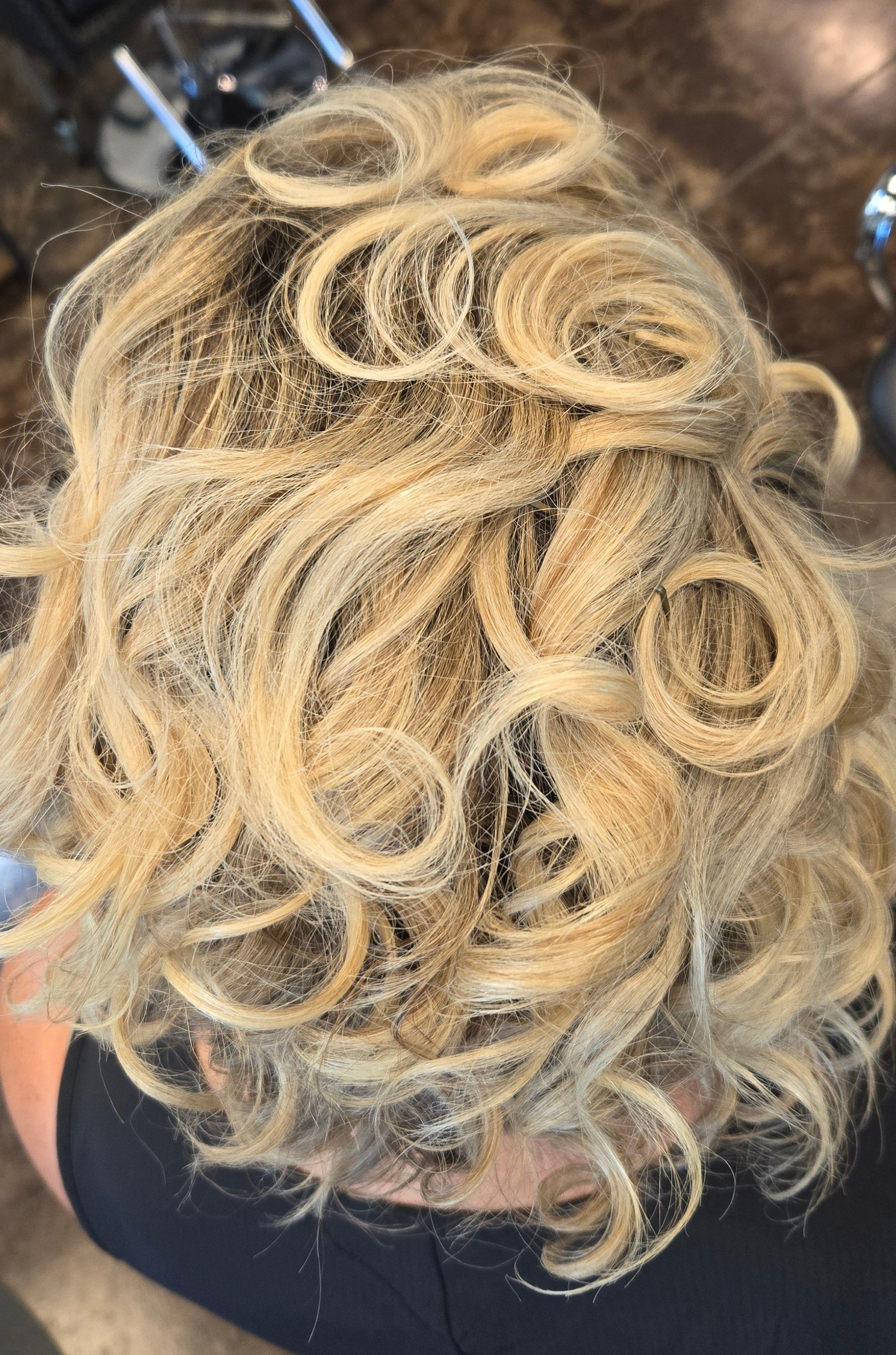 A woman with blonde curly hair is sitting in a chair in a salon.