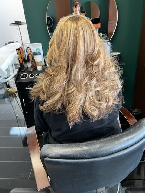 A woman with long blonde hair is sitting in a chair in a salon.