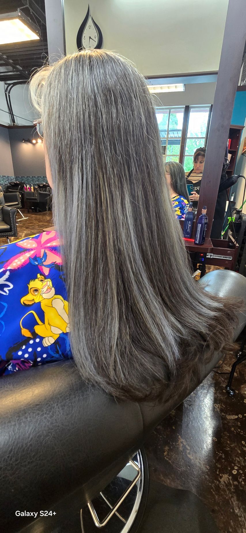 A woman with long gray hair is sitting in a chair at a hair salon.