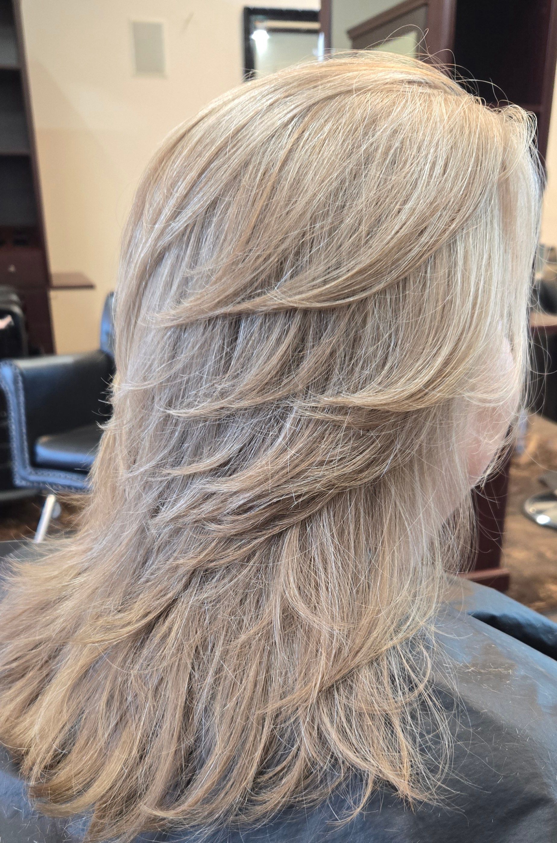 A woman with long blonde hair is sitting in a chair in a salon.