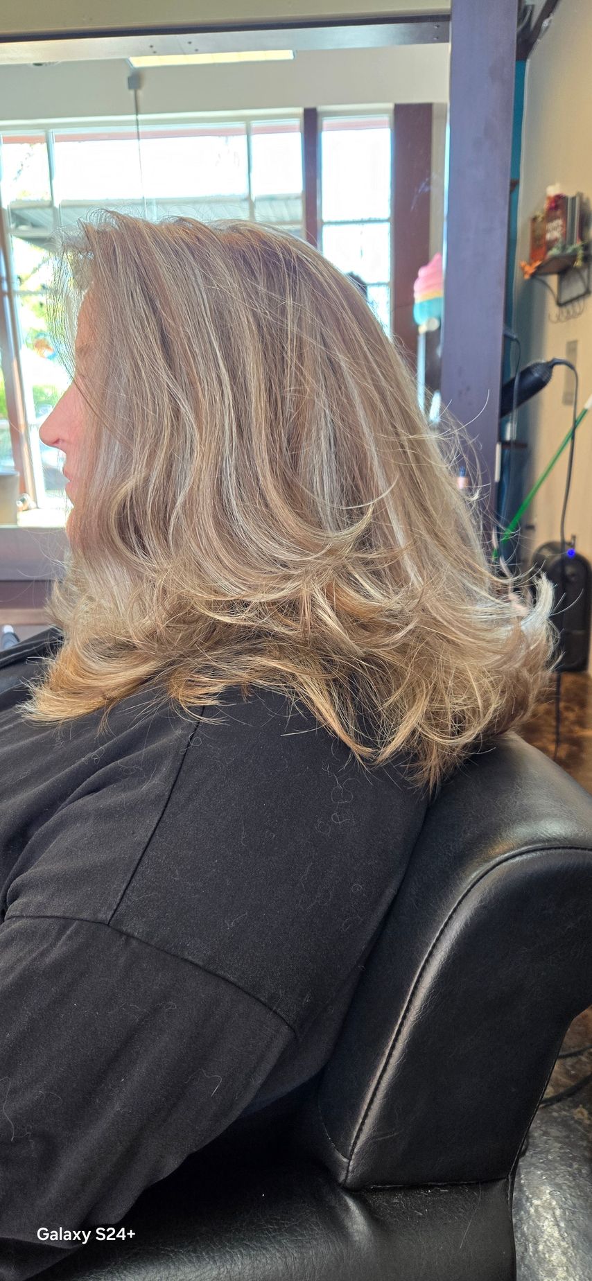 A woman with long blonde hair is sitting in a chair at a hair salon.