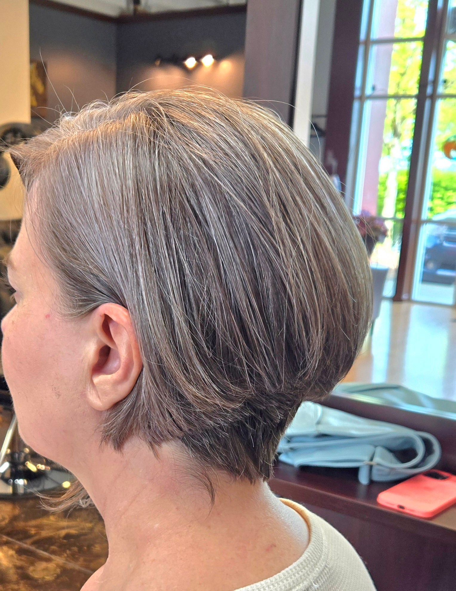 A woman with gray hair is getting her hair cut in a salon.