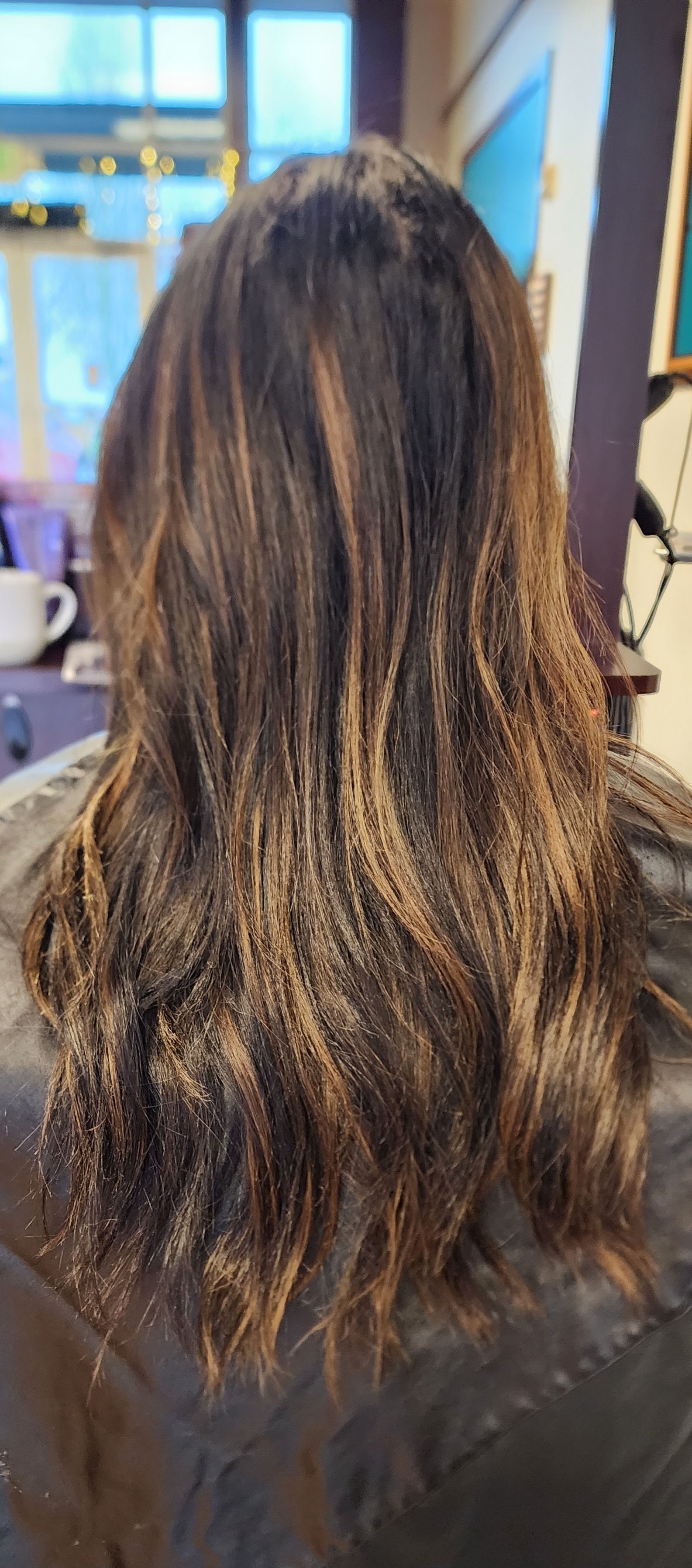 A woman with long brown hair is sitting in a chair in a salon.