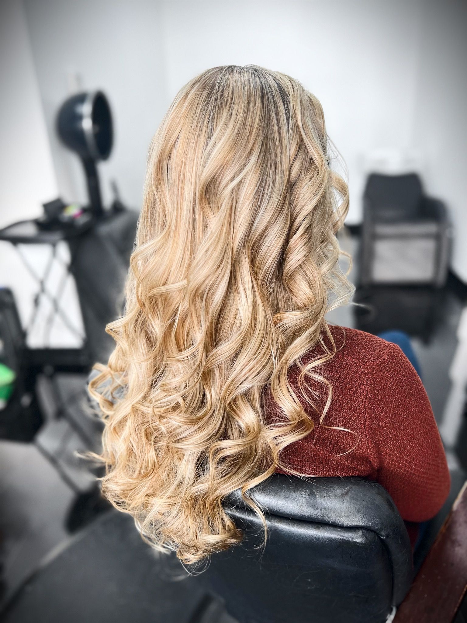A woman with long blonde hair is sitting in a chair in a salon.