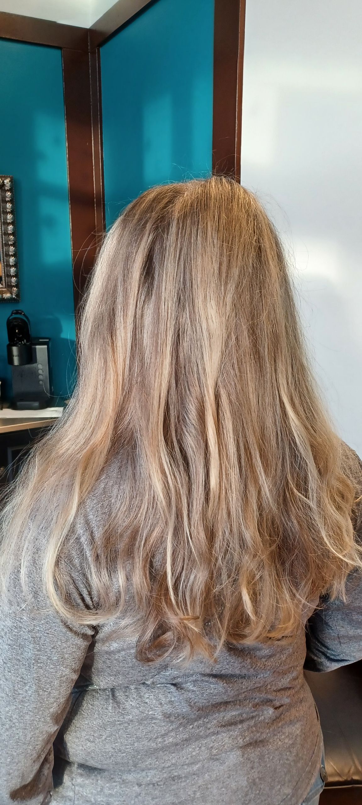 A woman with long blonde hair is standing in front of a mirror in a room.