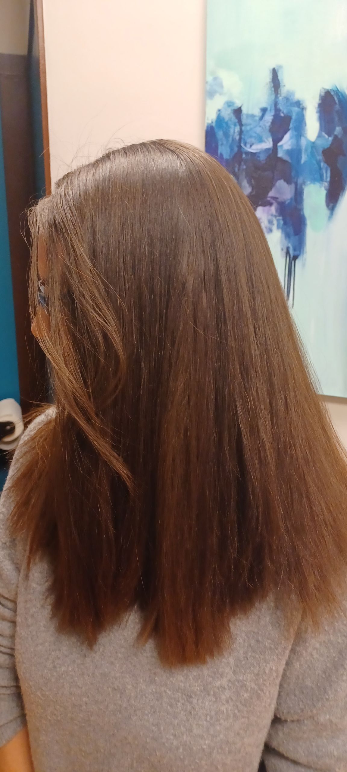 A woman with long brown hair is sitting in front of a painting.