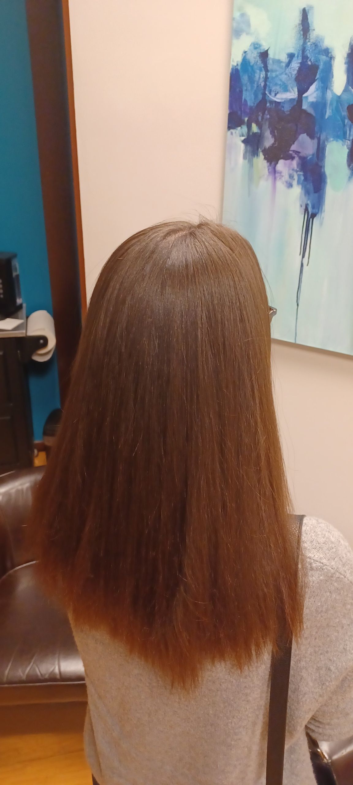 A woman with long brown hair is sitting in a chair in front of a painting.