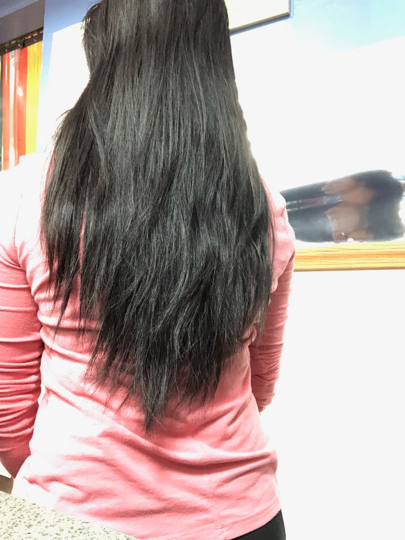 A woman with long black hair is standing in front of a mirror.