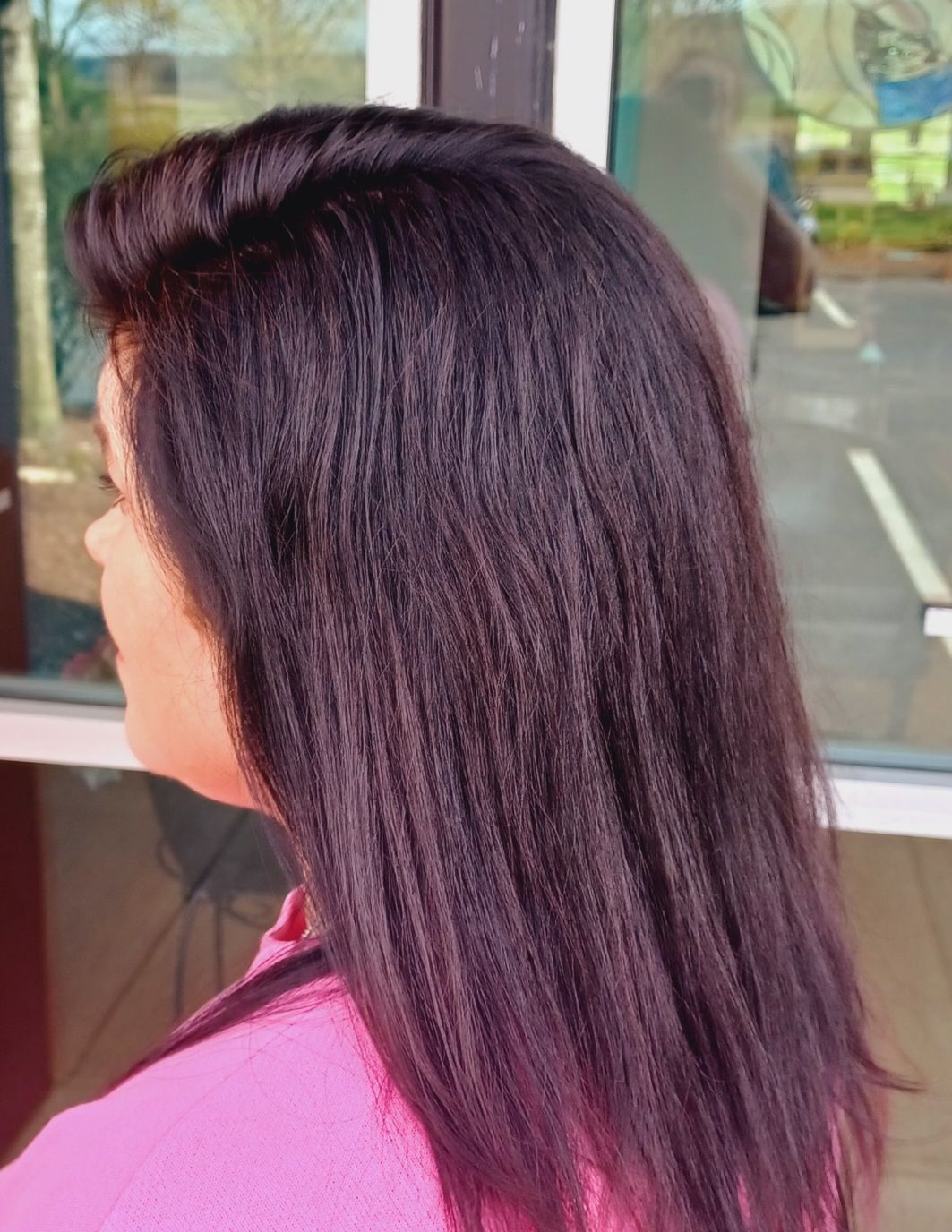 A woman with long dark hair is standing in front of a window.