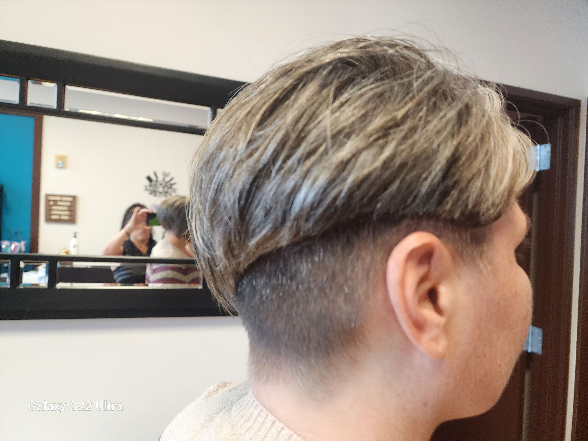 A woman with short hair is standing in front of a mirror.