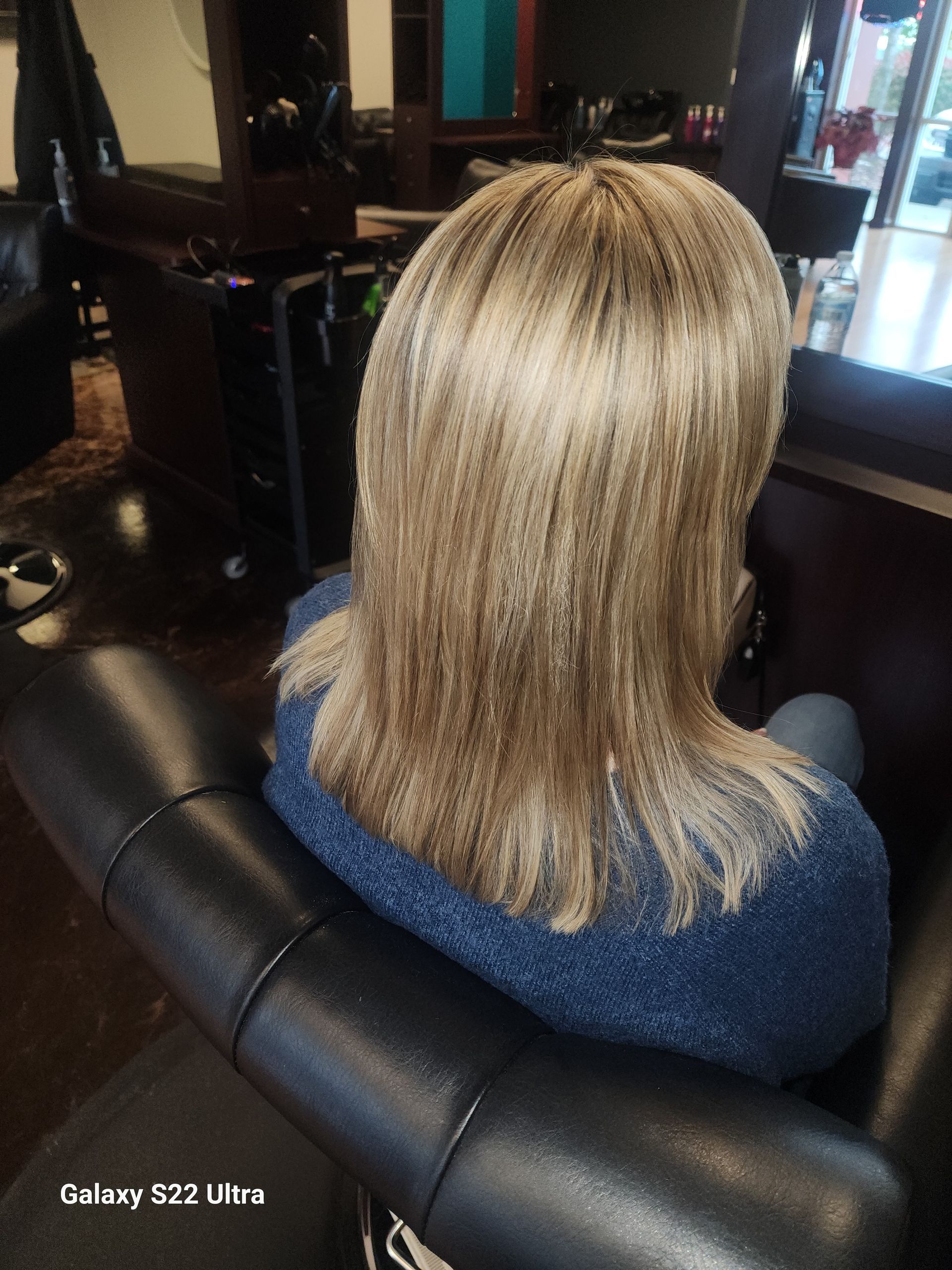 A woman with blonde hair is sitting in a chair in a salon.