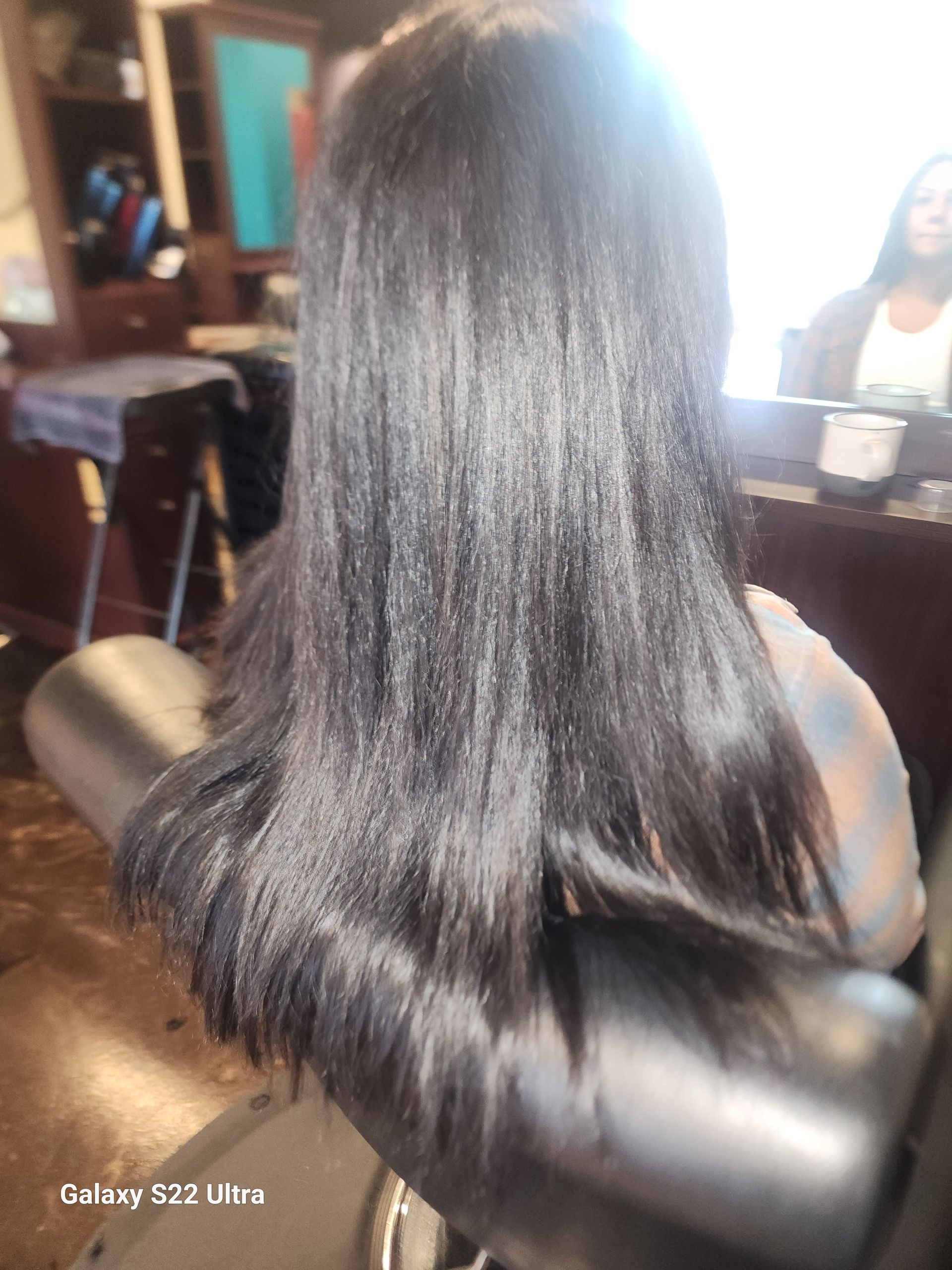 A woman with long black hair is sitting in a chair in a salon.