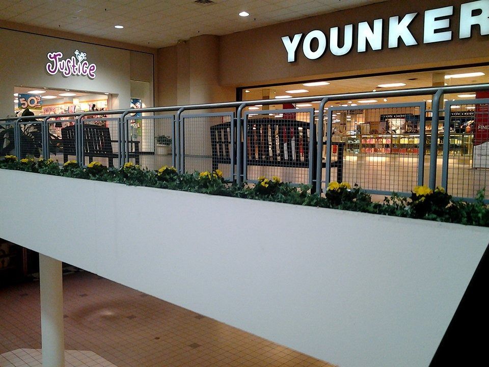 Interior of a mall with a Younker’s storefront and an empty upper-level walkway with railings and plants