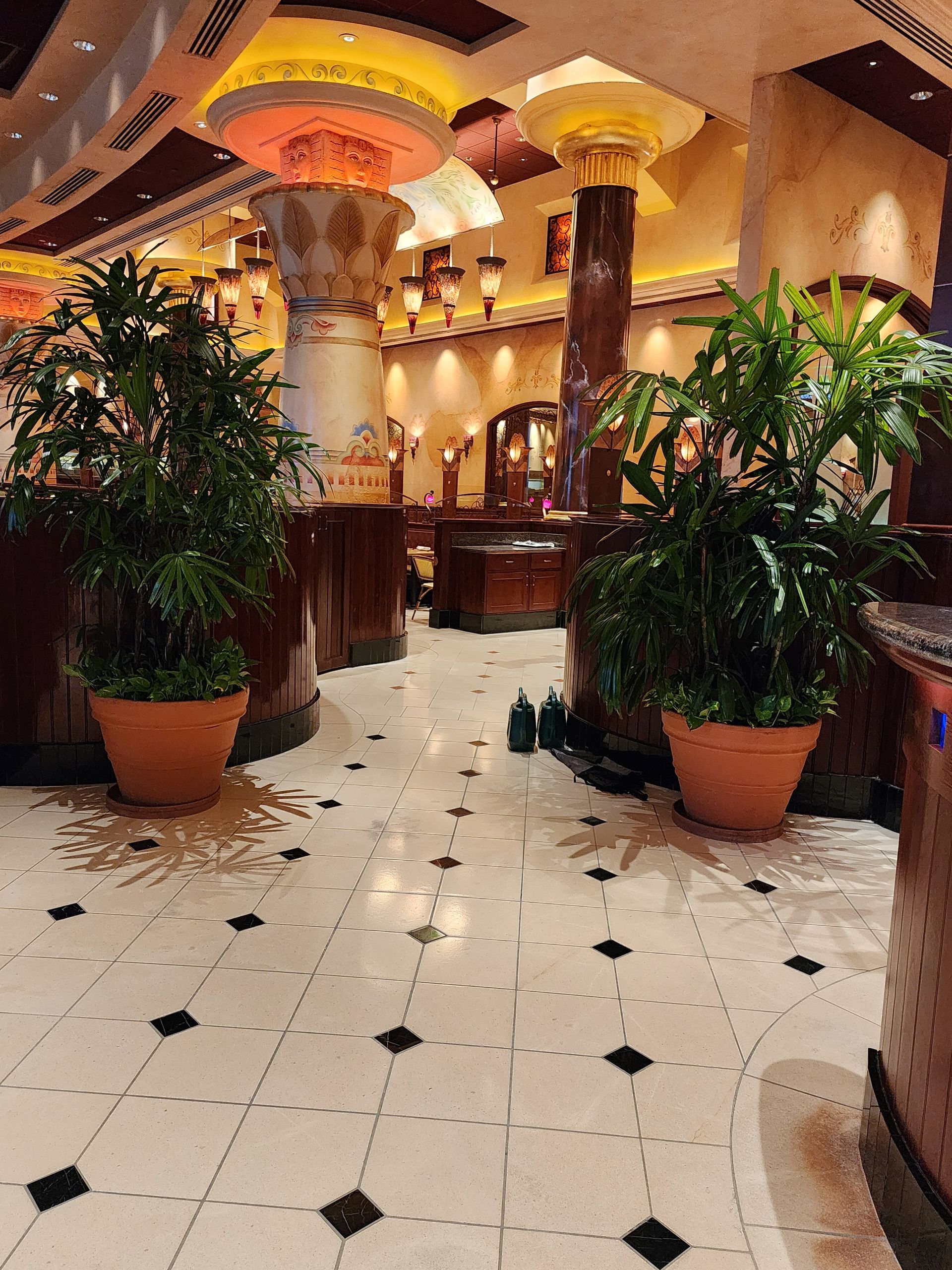 Elegant hotel lobby with white tiled floor, large potted plants, warm lighting, and ornate columns