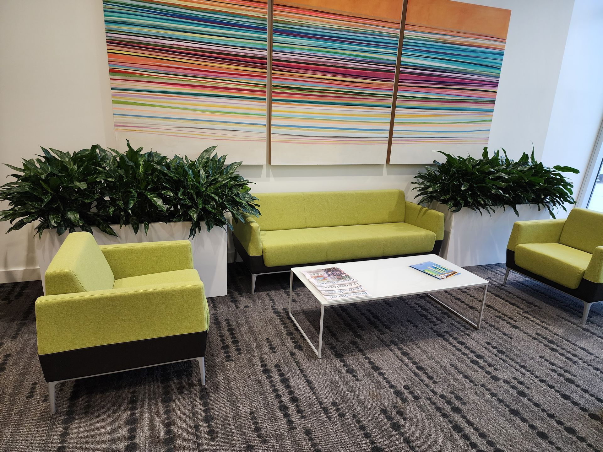 Modern lounge with lime-green chairs and sofa, white coffee table, plants, and colorful abstract wall art.