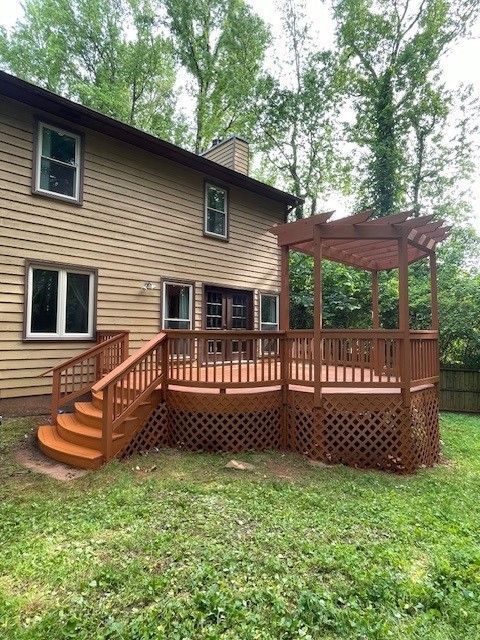 Back deck with stairs, lattice skirting, and gazebo-style pergola on a beige house in a grassy yard.
