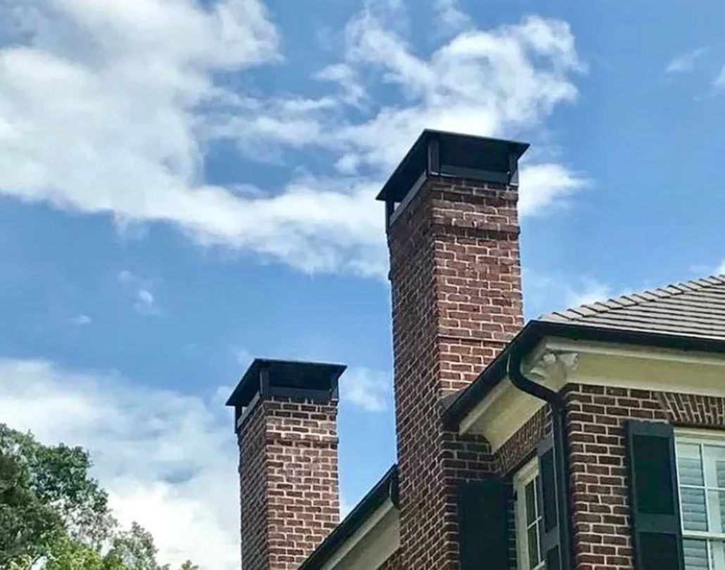 Brick house roofline with two tall chimneys against a blue, partly cloudy sky.