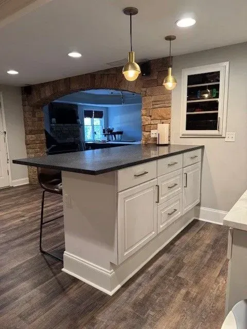Modern kitchen with a white island, dark countertop, pendant lights, and wood flooring