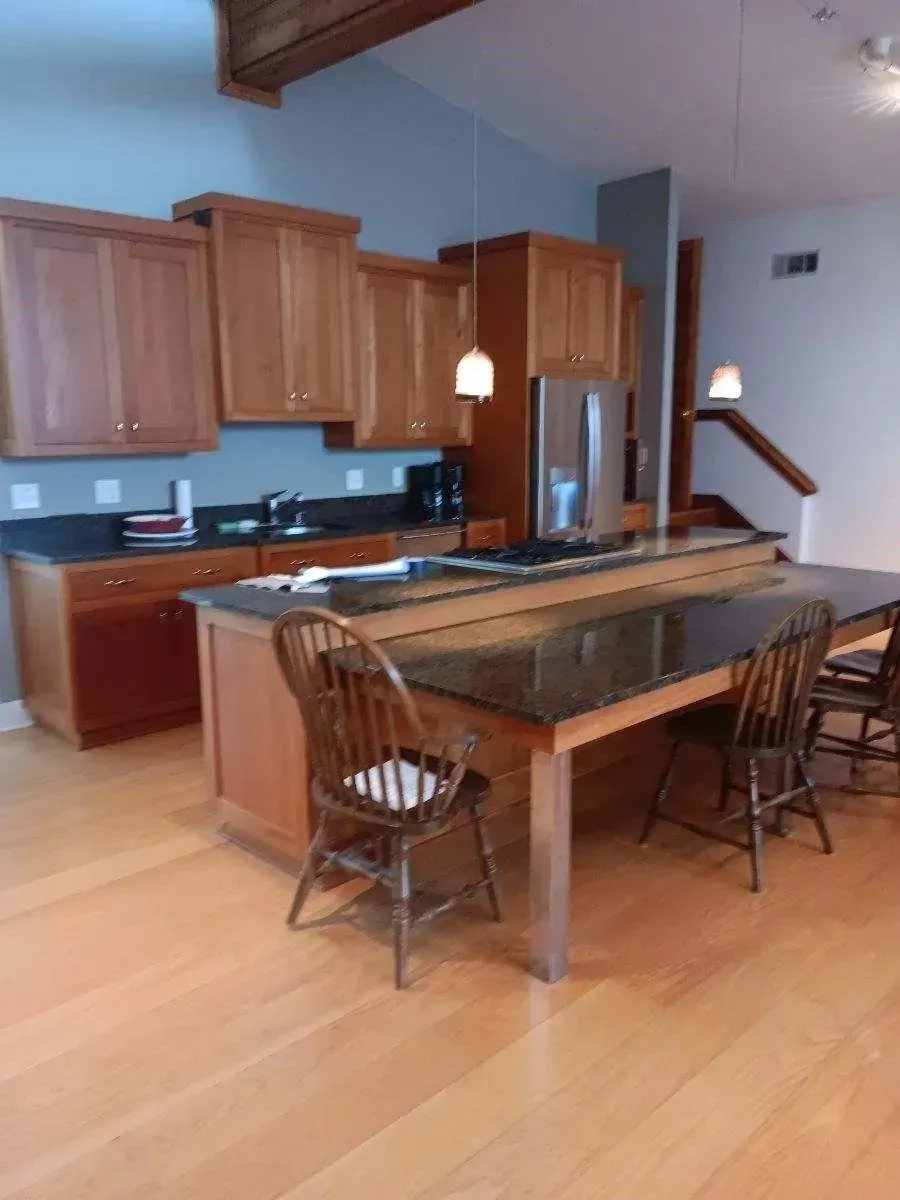 Open kitchen with wood cabinets, island, dining chairs, and high ceiling.