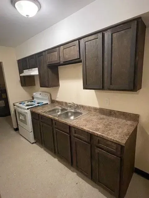 Small kitchen with dark wood cabinets, brown countertops, white stove, and stainless sink.