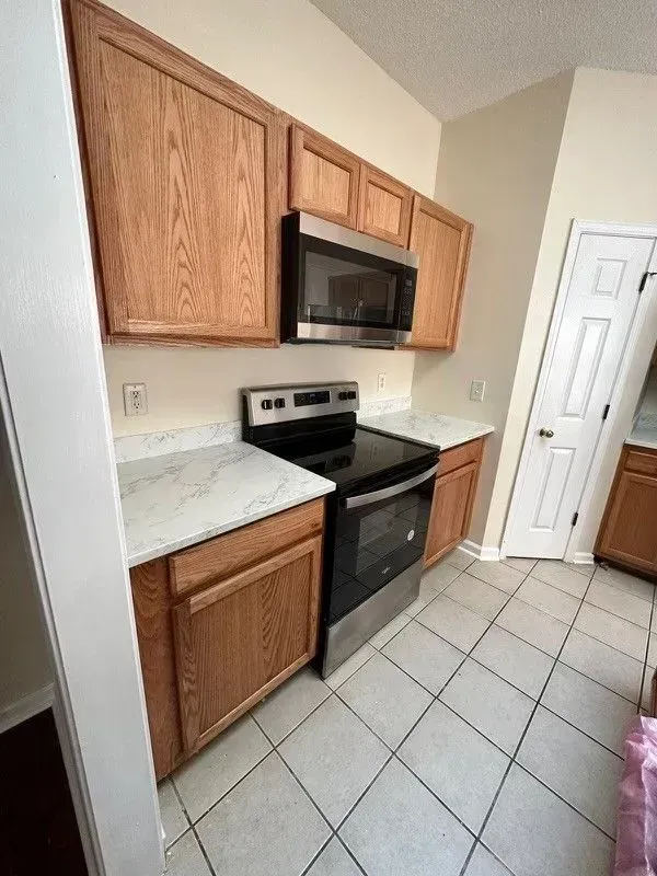 Small kitchen with wood cabinets, black stove and microwave, light countertops, and tiled floor.