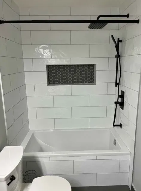 Accessible bathroom with walk-in tub, white tile walls, and black shower fixtures