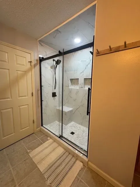 Bathroom with glass shower enclosure, white tile walls, and striped bath mat on beige floor.