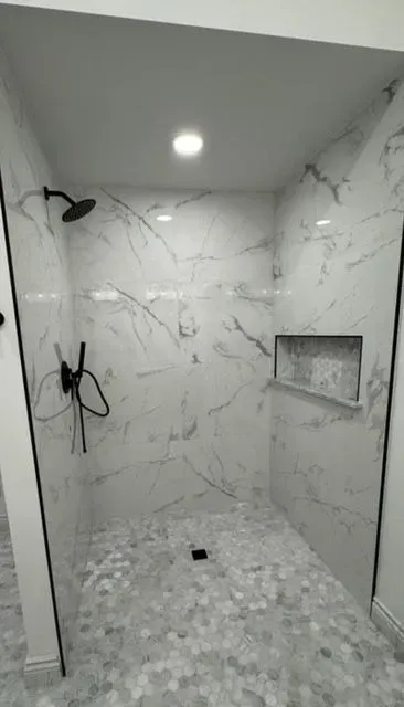 Marble-tiled walk-in shower with two black showerheads, recessed shelf, and pebble floor.