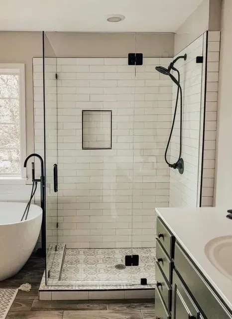 Modern bathroom with white-tile walk-in shower, black fixtures, and a freestanding tub by a window