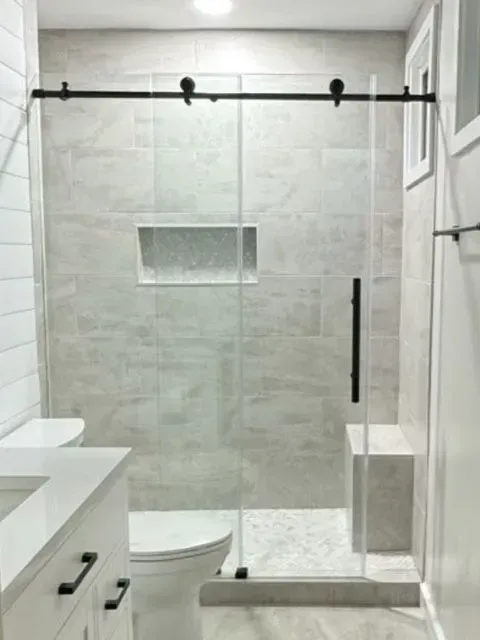 Modern white bathroom with glass shower enclosure, toilet, and vanity sink