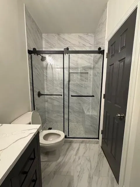 Modern bathroom with marble tile, black vanity, toilet, and glass walk-in shower.