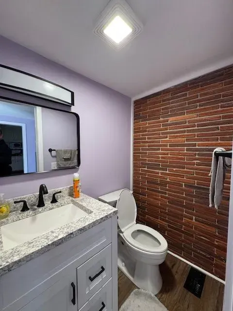 Small bathroom with vanity, sink, toilet, mirror, and brick accent wall.