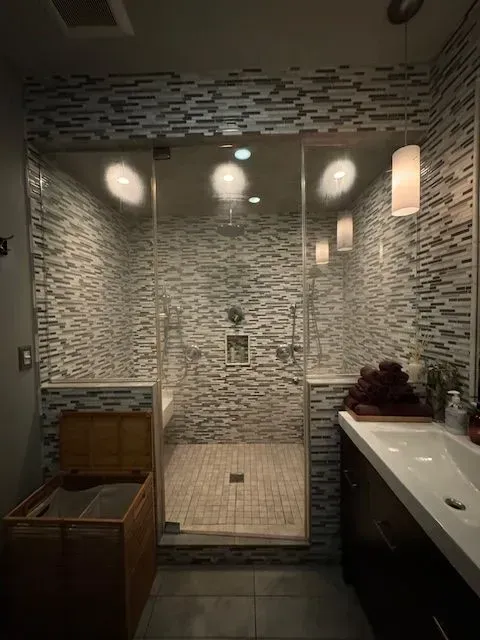 Modern bathroom with mosaic tile walls, glass shower, wooden tub, and white vanity sink
