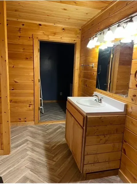 Wood-paneled bathroom with a sink vanity, large mirror, and open doorway to a dark adjoining room.