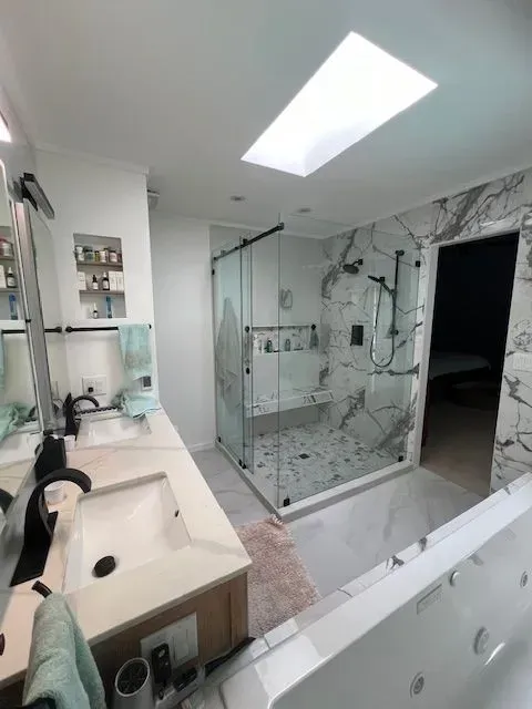 Modern bathroom with glass shower, marble tile, double sink, and skylight.
