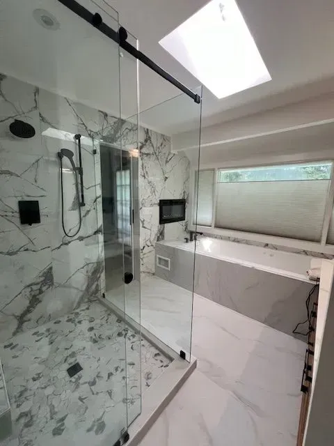 Modern bathroom with glass shower enclosure, marble-pattern walls, and skylight window