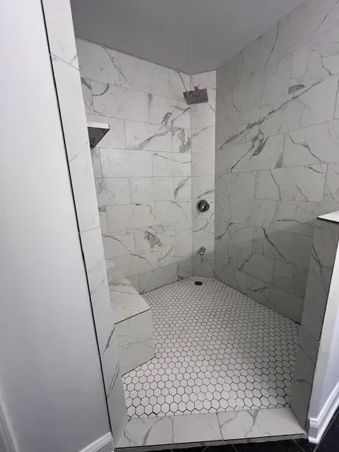 Small marble-tiled shower with white hexagon floor and built-in corner shelves