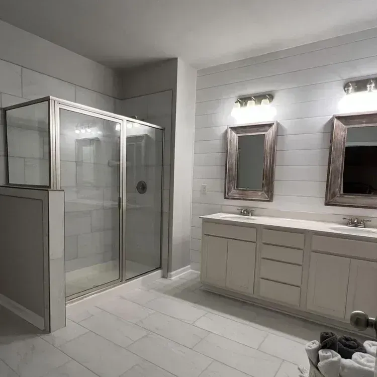 Modern white bathroom with glass shower, double vanity, mirrors, and tiled floor