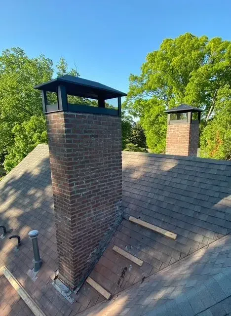 Two brick chimney stacks on a shingled roof under a blue sky