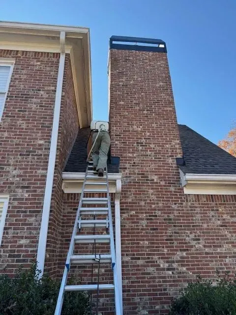 Worker on ladder repairing a brick chimney on a house exterior