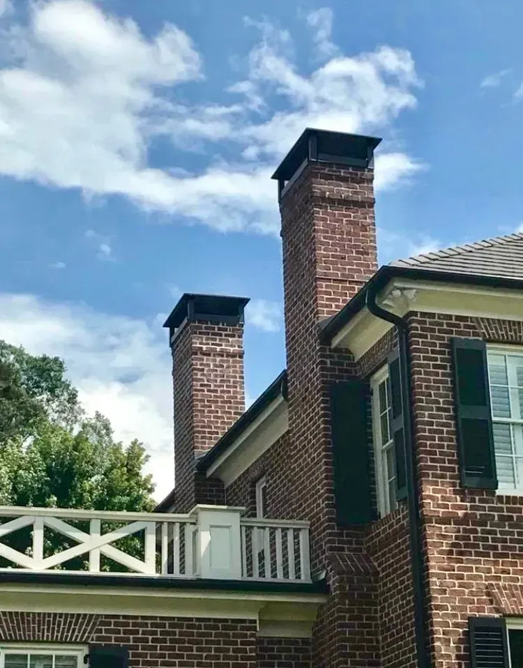 Brick house with two tall chimneys and a white porch railing under a blue sky