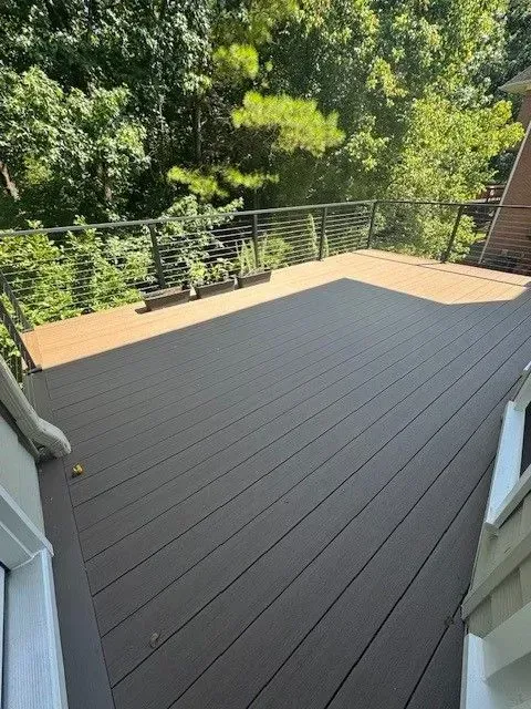 Wooden deck with black railing overlooking green trees in bright daylight